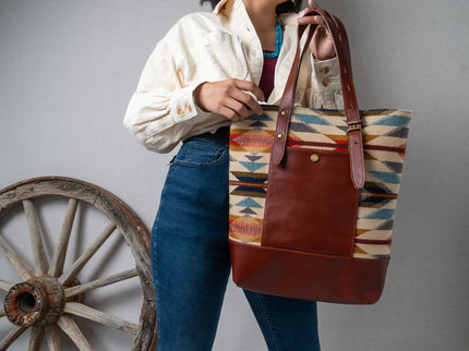 Young Navajo women holding a Pendleton brown leather tote bag with a rustic wheel in the background