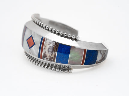 A silver bracelet with geometric inlay patterns including lapis, mother-of-pearl, and abalone, accented with coral lines and polished silver beads.