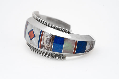 A silver bracelet with geometric inlay patterns including lapis, mother-of-pearl, and abalone, accented with coral lines and polished silver beads.