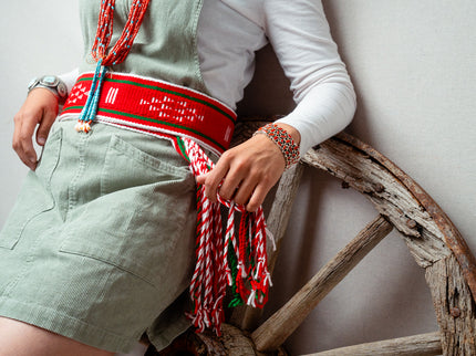 Navajo woman wearing a red sash belt and two bracelets, sitting on an old wooden wheel.