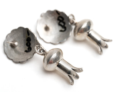 Close up of a pair of circular silver earrings with dangling silver shaped like flower stems a white background