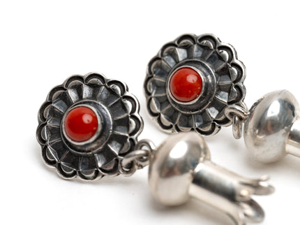 Close up of a pair of silver earrings with a single coral stone in the center of silver shaped like a blossom on a white background