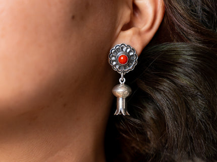Close-up of a silver earring with a red gemstone worn by a person.