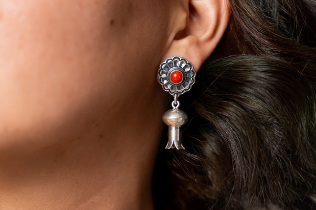 Close-up of a silver earring with a red gemstone worn by a person.