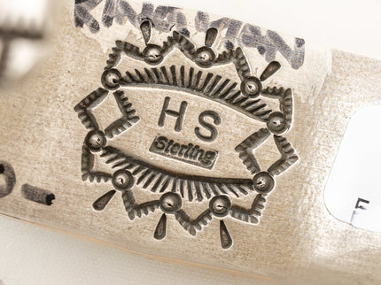 Close-up of a silver artist stamp with 'HS Sterling' engraving on a white background