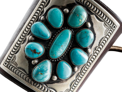 Close up of a dark brown leather bow guard with nine turquoise stones on a silver plate with stamp work on a white background