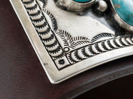 Close up of the intricate hand stamp work on the silver portion of a dark brown leather bow guard with nine turquoise stones