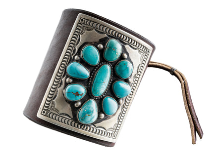 Dark brown leather bow guard with nine turquoise stones on a silver plate with stamp work on a white background