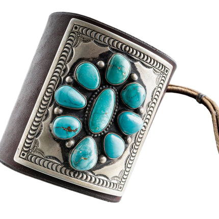 Dark brown leather bow guard with nine turquoise stones on a silver plate with stamp work on a white background