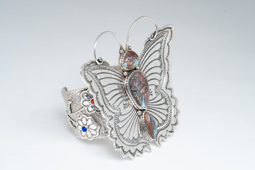 Angled front of bracelet showcasing a silver stamped butterfly with antennas and three turquoise stones. Side Cuff displays two flowers with one coral and one lapis stone.