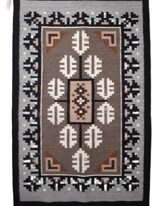 Traditional Navajo handwoven rug with a brown center and a grey and black borden featuring a Navajo geometric patterns
