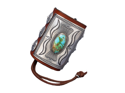 A richly detailed leather bowguard with a rectangular sterling silver plate showcasing flowing stamped patterns and a striking green-blue Sonoran Gold turquoise stone at the center. Decorated with dome-shaped silver conchos and secured with a dark brown leather tie.
