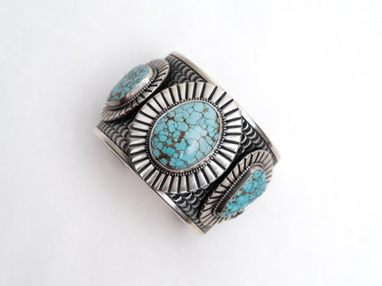 Top view of a silver cuff bracelet with 3 turquoise gemstones on a white background