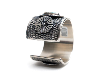Silver cuff bracelet with circular textured design on a white background