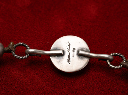 Close up of the name Matthew Charlie stamped into a silver necklace on a red background 