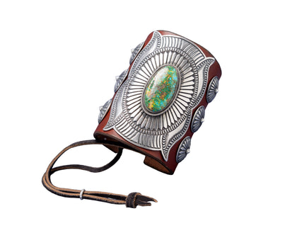 A handcrafted leather bowguard featuring an elaborate stamped sterling silver overlay with a radiant sunburst design, centered around a vibrant Sonoran Gold turquoise cabochon. Accented with scalloped conchos on the sides and a brown leather strap for fastening.