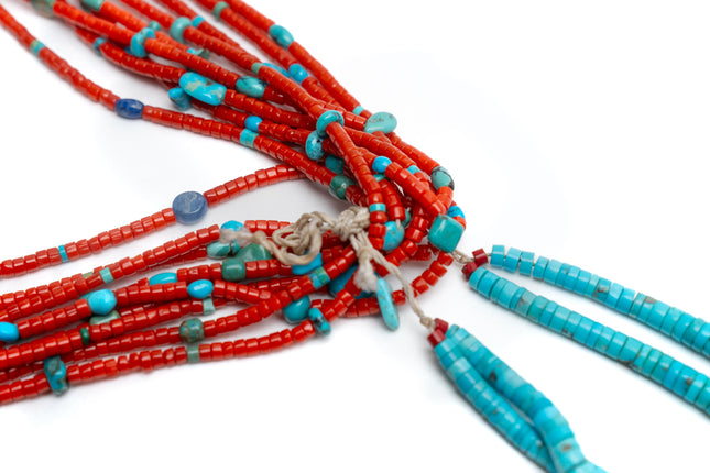 Close up view of a single Native American necklace with nine strands of Mediterranean coral with sleeping beauty, Royston and Kingman Turquoise stones, and Lapis on a white background