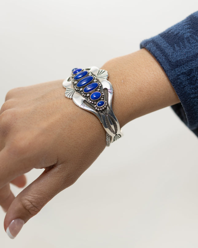 Model wearing a silver stamped bracelet with blue stones on a plain background