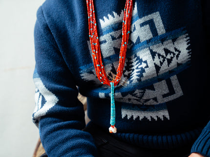 Person wearing a blue Pendleton sweater with a coral jacloo necklace.