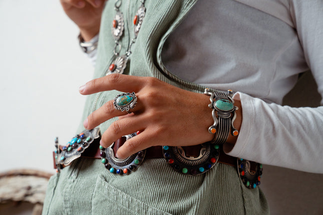 Navajo woman wearing multiple pieces of jewelry including an old-fashioned  Turquoise ring, a silver bracelet, and a concho on a light background