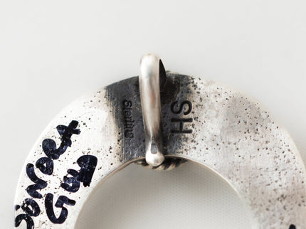Closeup of Herman Smith hallmark "HS" and the words "sterling" stamped on the back of a silver pendant 