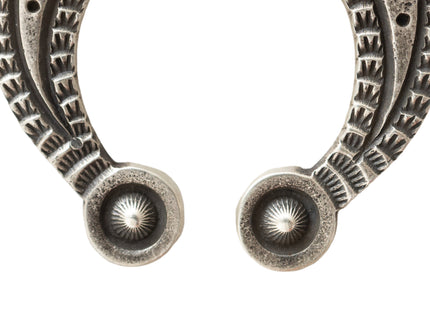 Closeup of Silver u-shpaed pendant tips intricate stamped designs on a light background