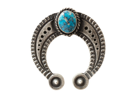 Silver u-shaped jewelry piece with a turquoise stone and stamp work on a light gray background