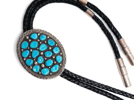Bolo tie with 17 Turquoise stones on a round silver center with black leather cord on a white background