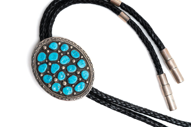 Bolo tie with 17 Turquoise stones on a round silver center with black leather cord on a white background
