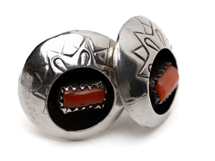 Pair of vintage Native American circular silver and coral shadow box earrings leaning against each other on a white background