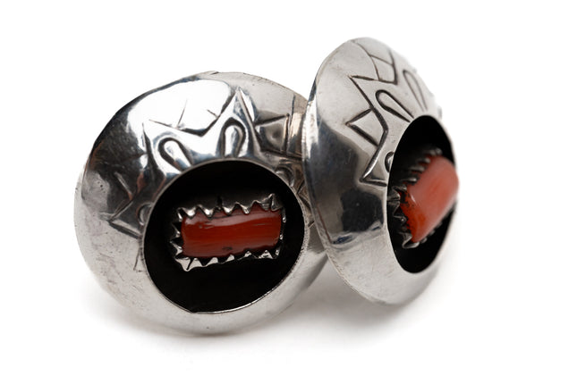 Pair of vintage Native American circular silver and coral shadow box earrings leaning against each other on a white background