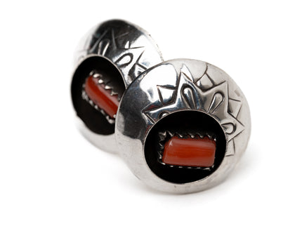 Pair of circular silver and coral shadow box stud earrings leaning against each other on a white background