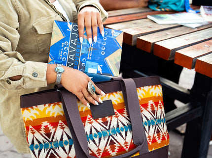 A Navajo female student is putting a tote bag by Pendleton and placing a book inside of it