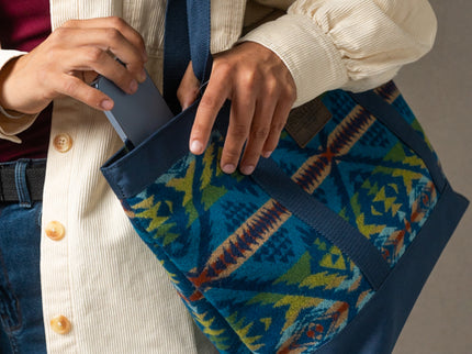 Person holding a blue Pendleton bag with geometric pattern and pulling out a blue phone from the bag