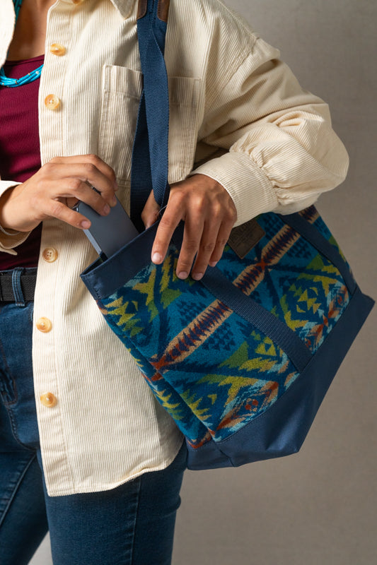 Person holding a blue Pendleton bag with geometric pattern and pulling out a blue phone from the bag