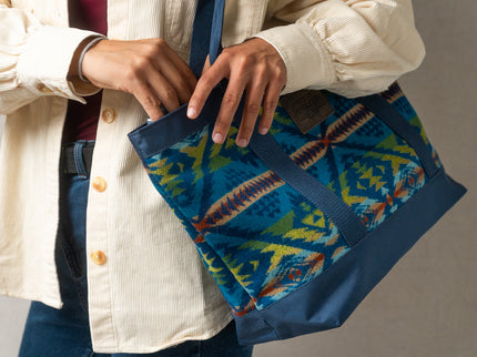 Person wearing a cream color Levi button up shirt is holding a blue and multicolored Pendleton patterned bag