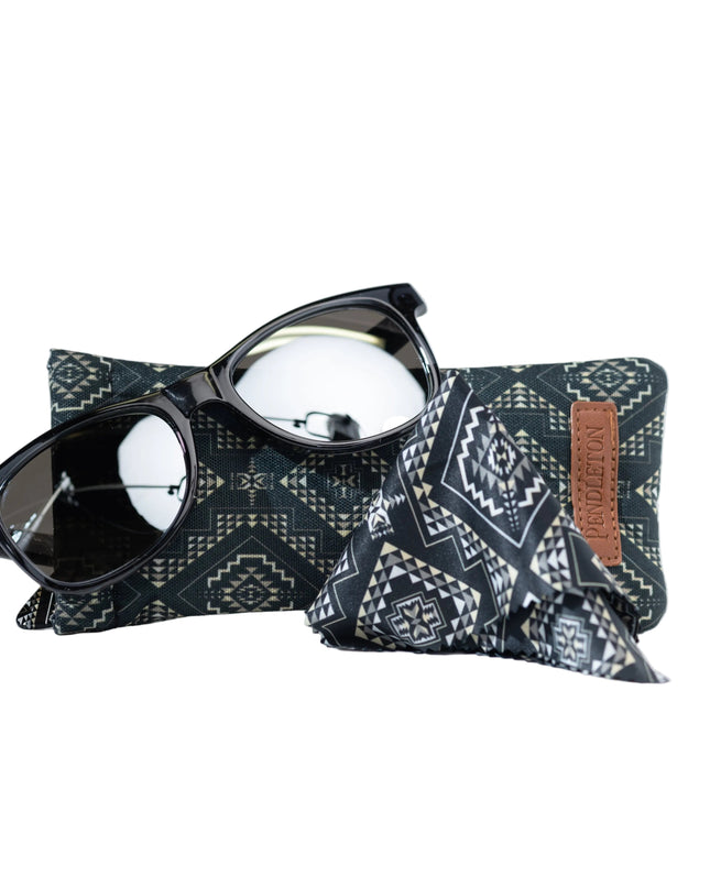 Pendleton dark grey sunglasses lay on a Pendleton patterned dark teal sunglasses case with a brown leather Pendleton label on a white background