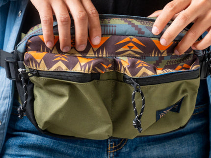 Two hands holding a Pendleton green patterned waist bag with a visible brand logo.
