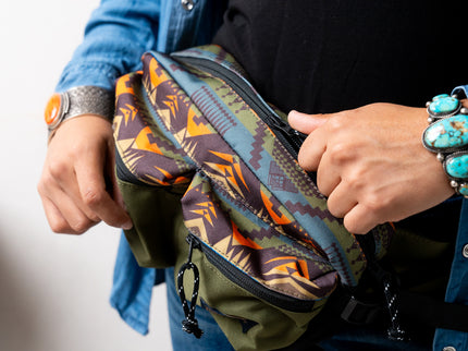 Person holding a Pendleton patterned bag with colorful designs, wearing a blue jacket and turquoise bracelet.