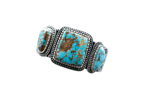 Top of a silver bracelet with three Royston Turquoise stones, by Navajo Silversmith Matthew Charley, with a solid white background. 