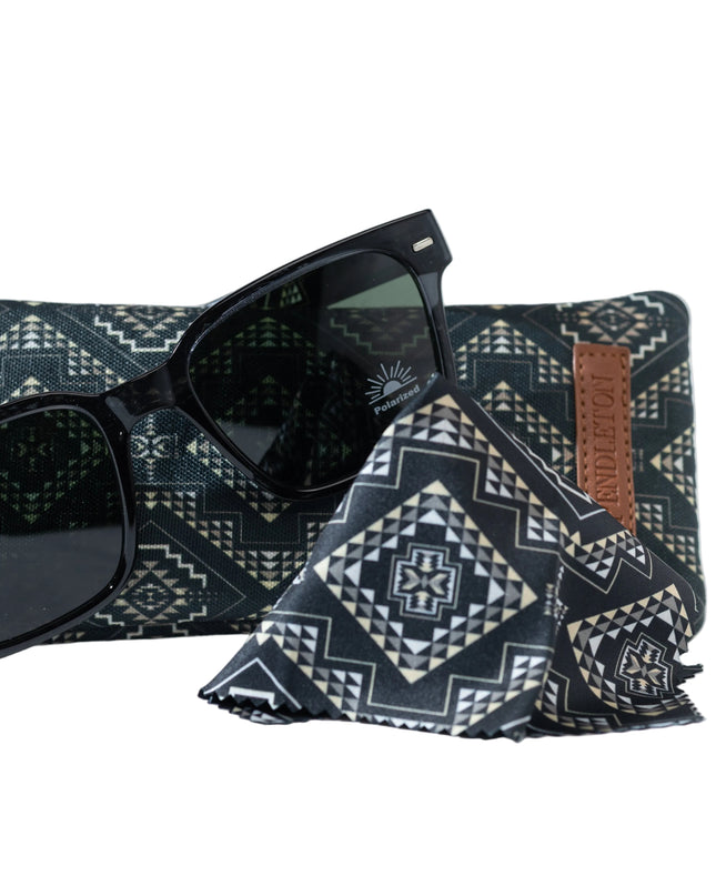 Black sunglasses on leaning on patterned Pendletong  pouch and lens wipe against a white background