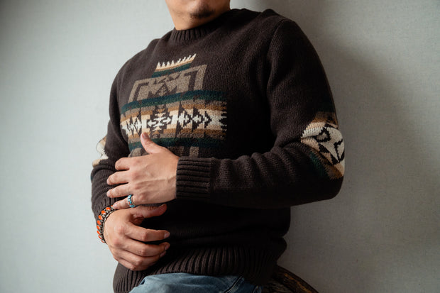 Navajo male wearing a dark brown sweater with Chief Joseph pattern, standing against a plain background