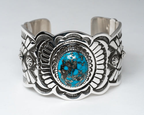 A silver-stamped cuff bracelet featuring a central Persian turquoise gemstone, with intricate hand-stamped designs around it.