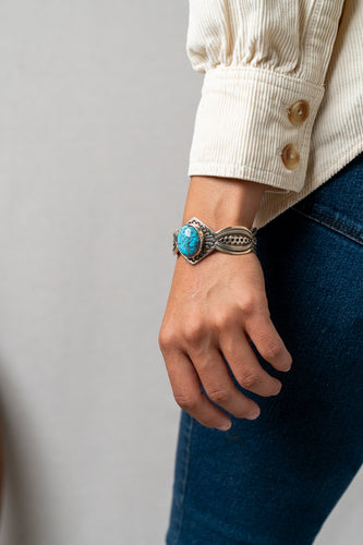 Hand wearing a silver Terry Martinez bracelet with a turquoise stone against a neutral background