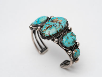 Top view of a Native American bracelet bracelet with one large turquoise stone in the center with 2 more smaller turquoise stones on each side on a white background