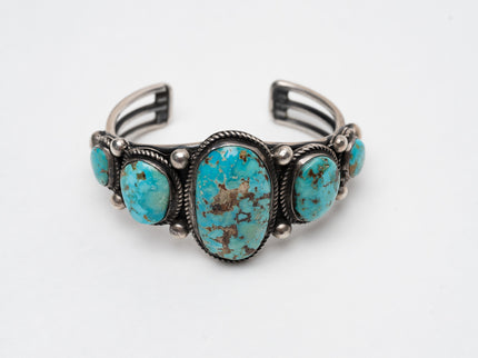 Native American bracelet with one large turquoise stone in the center with 2 more smaller turquoise stones on each side on a white background
