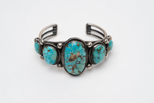 Native American bracelet with one large turquoise stone in the center with 2 more smaller turquoise stones on each side on a white background