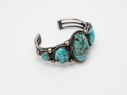 Native American silver bracelet with one large turquoise stone in the center with 2 more smaller turquoise stones on each side on a white background