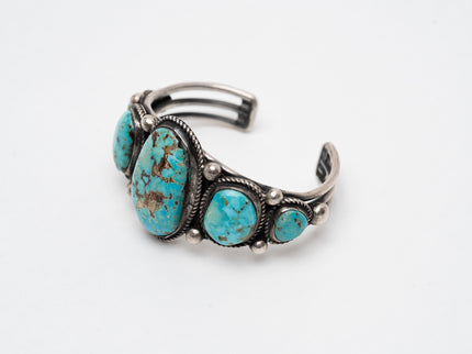 Native American bracelet with one large turquoise stone in the center with 2 more smaller turquoise stones on each side on a white background