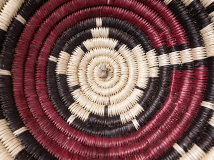 A vintage Navajo coiled basket with a starburst pattern in natural, red, and black tones, center close up of basket.